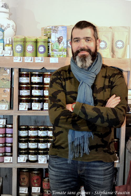 Bruno, alias Jean de la Tomate, posant devant des étagères de produits locaux.